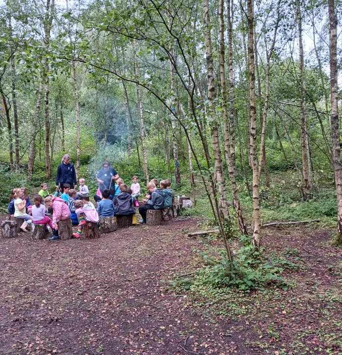 Forest school kids gather round a fire with the leader standing in the middle