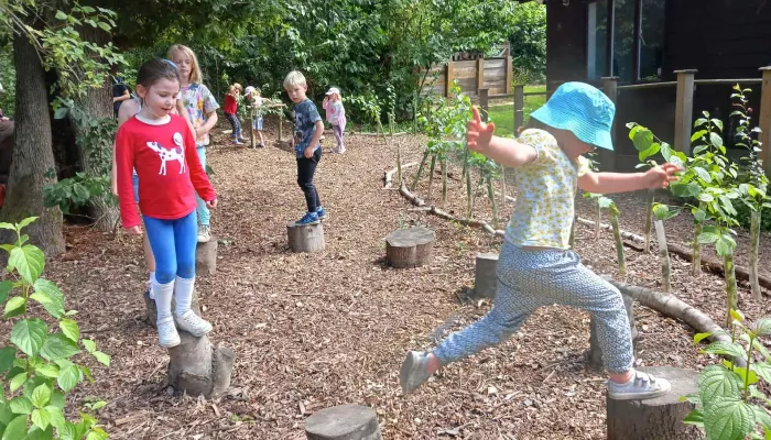 Children at a Kent Wildlife Trust holiday club jumping on stepping-stone logs.