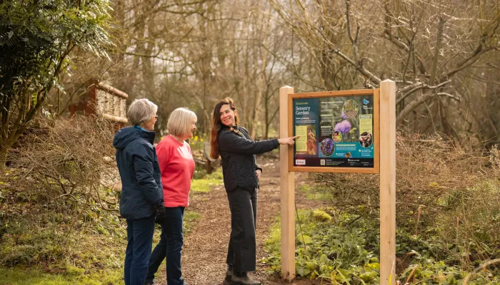 Three people standing and looking at a sign in a nature reserve.