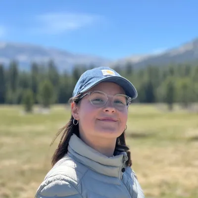 Celena Sabin-Dawson, a person in a blue hat, stood in front of a mountainous landscape.