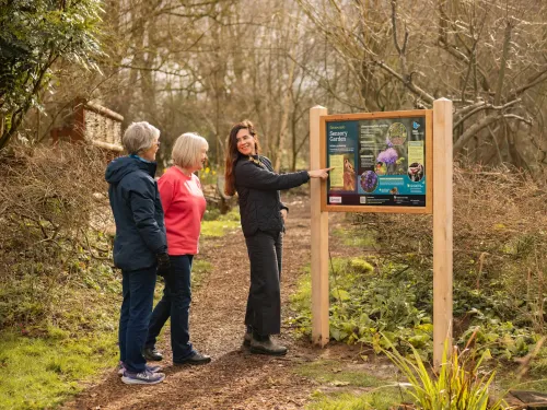 Three people standing and looking at a sign in a nature reserve.